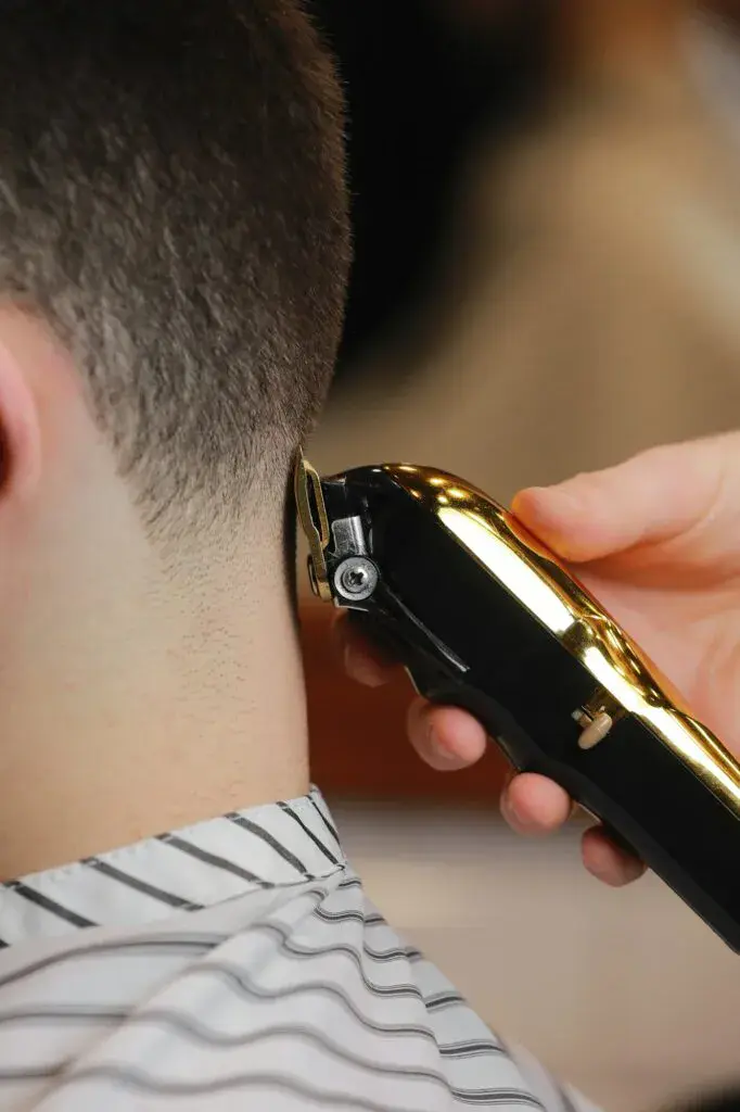 Hairdresser, barber cutting the hair from the back of the client's head with a gold electric clipper